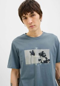 Grå bomulds T-shirt med korte ærmer, prydet med et grafisk design af palmetræer og tekst i kontrastfarver. Casual, afslappet pasform.