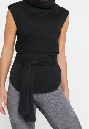 Ærmeløs sort top med høj halsudskæring og bredt bælte bundet om taljen, kombineret med grå teksturerede leggings.