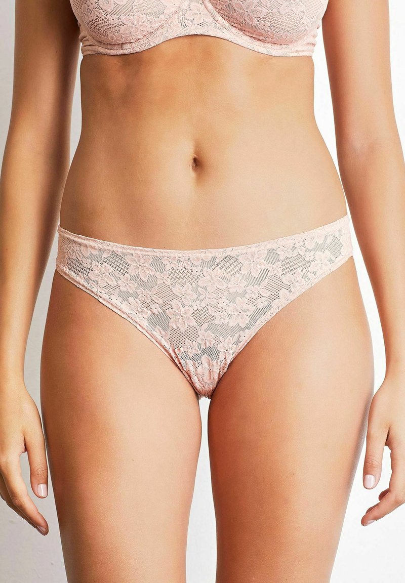 Slip de bikini din dantelă, de culoare roz deschis, cu modele florale și panouri semi-transparente. Prezintă o croială joasă și margini fără cusături pentru confort.