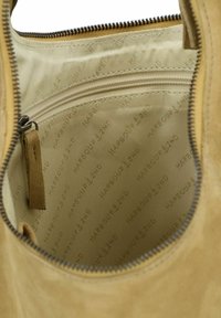 Interno della borsa in suede color tan con fodera in tessuto liscio e chiaro. Presenta una tasca con zip e un motivo a logo embossato in tutto il prodotto.