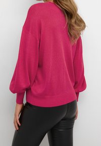 Pull tricoté fuchsia avec manches ballon, ourlet côtelé et texture. Associé à un pantalon noir ajusté, vu de dos.