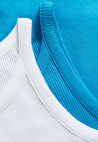 T-shirts de alças brancas e turquesa em sobreposição, com golas redondas e tecido texturizado. Cores contrastantes notáveis e padrões finos.