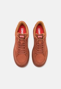 Sneaker in suede marrone con punta rotonda, lacci piatti e accentuazioni beige. Etichetta con logo sulla linguetta. Suola in gomma testurizzata. Soletta rossa.