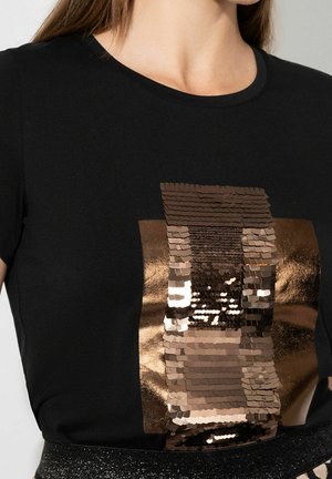 T-shirt noir avec un motif rectangulaire à paillettes brillantes dans des tons bronze et marron sur le devant.