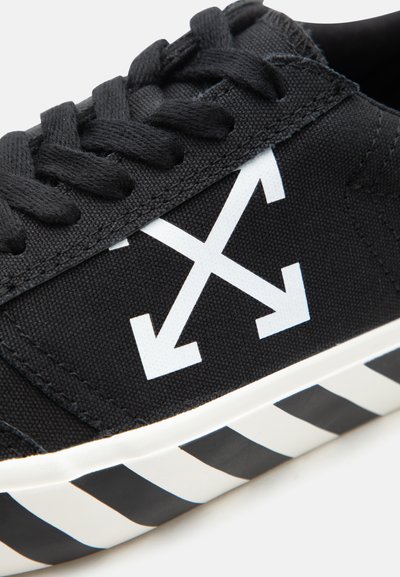 Μαύρο αθλητικό παπούτσι με λευκό λογότυπο διασταυρούμενων βελών στο πλάι και μοτίβο μαύρου-λευκού διαγωνίου ρίγες στην σόλα.