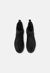 Bottines en daim noir avec bouts ronds, empiècements élastiques et semelles en caoutchouc texturé. Design minimaliste, avec languettes de traction à l'arrière.