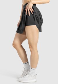 Zwarte skort met een geplooid ontwerp, middelhoge tailleband, gecombineerd met witte sneakers en sokken met zwarte letters.