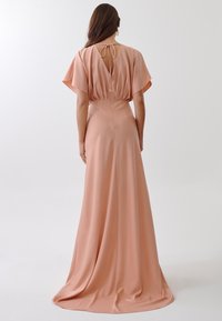 Peach-colored floor-length dress made of smooth fabric, featuring flutter sleeves, a tie-back closure, and a fitted waist.