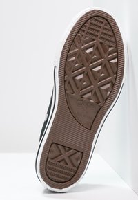 Semelle de chaussure de sport en caoutchouc noir avec un motif de bande de roulement géométrique, bords blancs et détail embossé "Converse All Star". La texture est lisse avec des rainures.