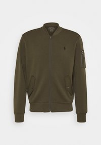 Bomber bunda v olivově zelené barvě z měkké tkaniny. Má přední zip, žebrované manžety, dvě přední kapsy a kapsu na zip na rukávu.