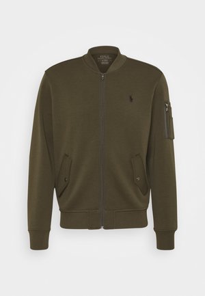 Bomber bunda v olivově zelené barvě z měkké tkaniny. Má přední zip, žebrované manžety, dvě přední kapsy a kapsu na zip na rukávu.