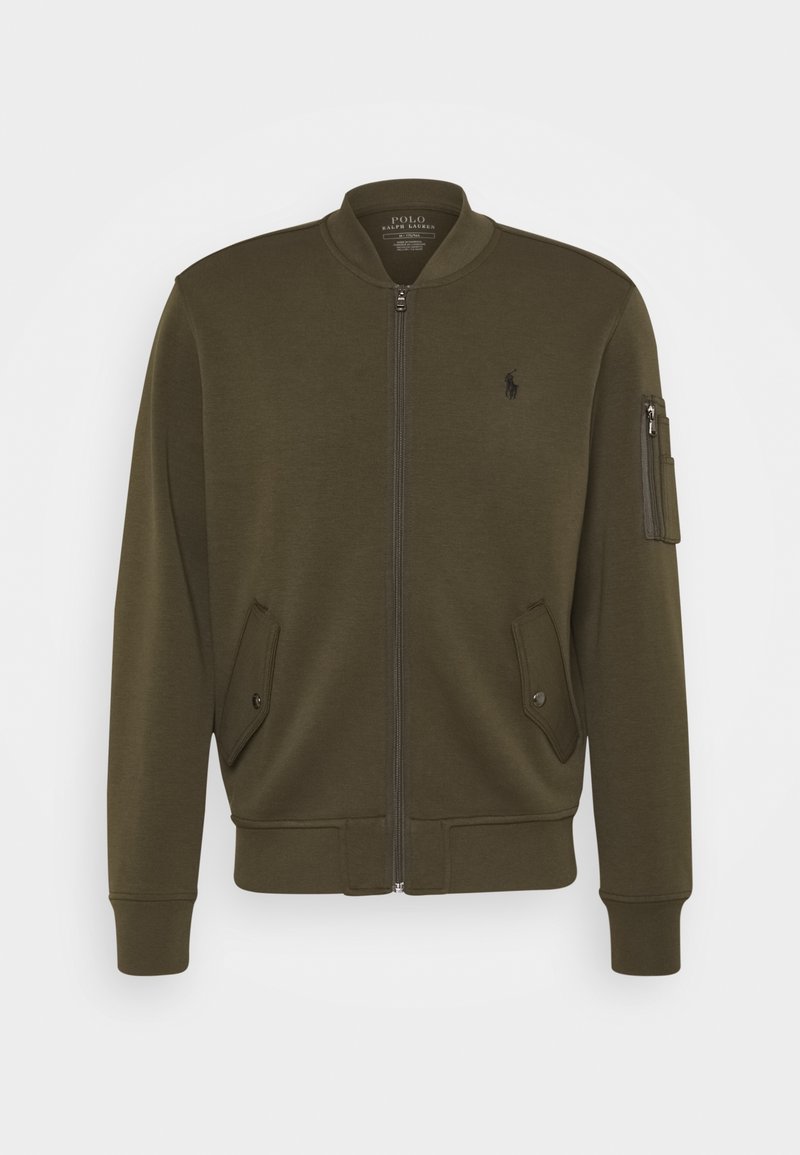 Bomber bunda v olivově zelené barvě z měkké tkaniny. Má přední zip, žebrované manžety, dvě přední kapsy a kapsu na zip na rukávu.