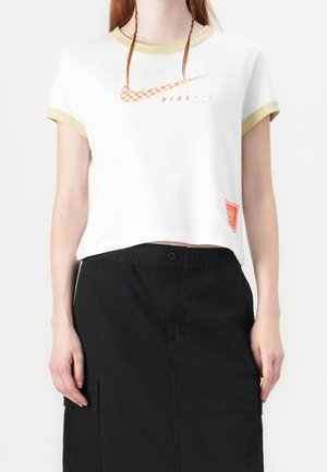 Biały bawełniany t-shirt z krótkimi rękawami wykończonymi bladożółtą lamówką, z pomarańczowym, kratkowanym logo Nike oraz czerwoną metką Nike na dole.