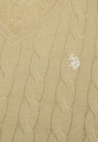 Pulover bej cu model tricotat în cablu și design cu decolteu în V. Prezintă un model texturat și un logo brodat alb pe partea stângă a pieptului.