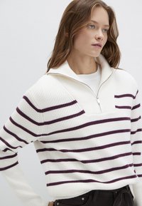 Weißer Rippstrickpullover mit maroonfarbenen horizontalen Streifen, ausgestattet mit einem halben Reißverschluss und einer Fronttasche. Lässiger Schnitt mit langen Ärmeln.