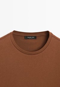 T-shirt marron à manches courtes avec un col rond et un tissu texturé. Présente une étiquette avec l'inscription "Massimo Dutti".