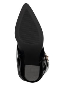 Zwarte schoenzool met puntige neus en textuur voor grip op hiel en voorkant, voorzien van een riem met gesp aan de zijkant op een glad leren bovenwerk.