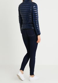 Navy blue, shiny puffer jacket with a high collar, paired with dark jeans and white sneakers, viewed from the back.