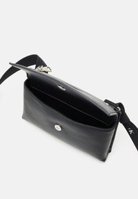 Czarna skórzana torebka na ramię o gładkiej fakturze, z zamknięciem na zamek błyskawiczny, zatrzaskiem oraz materiałowym paskiem z logo. Wnętrze jest przestronne i niepodszewkowane.