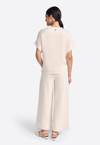 Top beige oversize con maniche corte e scollatura rotonda, abbinato a pantaloni a gamba larga. Tessuto liscio con dettagli minimi.