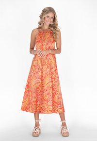 Bunt gemustertes Paisley-Midi-Kleid in Orange und Gelb, mit Halsband-Design und fließendem Rock. Kombiniert mit leichten Espadrilles.