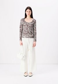 Top de manga larga a rayas en tonos marrón y blanco, combinado con pantalones de pierna ancha blancos y texturizados, complementado con un pequeño bolso blanco y zapatos.