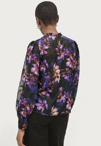 Schwarze, durchsichtige Bluse mit einem lebhaften Blumenmuster in Lila und Orange, ausgestattet mit Puffärmeln und einem Schlüsselloch-Ausschnitt im Rücken.