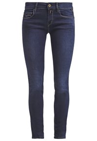 Jeans ajustados de denim azul oscuro con costuras tonales, diseño de cinco bolsillos, cierre de botón frontal y cremallera. Textura suave, forma ajustada.