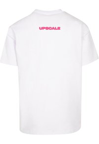 Hvid bomuld t-shirt med korte ærmer, med "UPSCALE" trykt i pink på den øverste ryg. Klassisk crew neck-design.