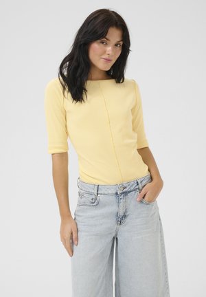 Geel geribbeld aansluitend topje met driekwartmouwen, voorzien van een centrale naad, gecombineerd met lichtblauwe wijde jeans.