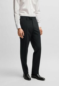 Pantaloni neri con una vestibilità su misura, realizzati in tessuto liscio. Presentano un davanti piatto, passanti per cintura e una piega lungo le gambe anteriori.