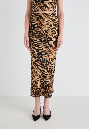Jupe midi imprimé léopard en tissu lisse, présentant une silhouette ajustée et une fente sur le côté. Le modèle porte des escarpins noirs à bout pointu.