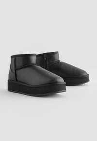 Schwarze Lederstiefeletten mit runder Zehenform, Reißverschluss und strukturiertem Gummisohle. Niedriges Profil mit minimaler Polsterung am Schaft.