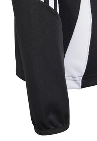 Melna sporta jaka ar baltām akcentiem un teksturētu audumu. Iezīmējas ar ribotu aproci un kontrastējošu dizainu gar roku.