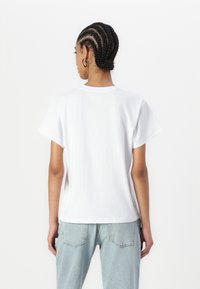 Tricou alb din bumbac, cu mâneci scurte, de tip crew neck și o croială relaxată. Asortat cu blugi din denim albastru deschis. Design minimalist, fără modele.