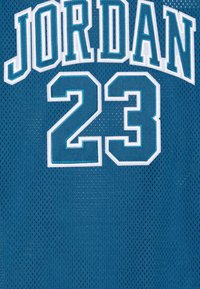 Tyrkysový basketbalový dres z síťoviny s bílým nápisem "JORDAN" a výrazným číslem "23" na přední straně. Má prodyšný materiál a volný střih.