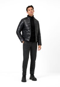 Schwarze Leder-Puffermantel mit Reißverschluss, strukturiertem Stoff, kombiniert mit einem schwarzen Strickrollkragenpullover und grauen Wollhosen, abgerundet mit schwarzen Stiefeln.
