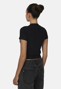 Czarny crop top z krótkimi rękawami, wykonany z lekkiego materiału. Posiada subtelne logo z tyłu. W połączeniu z szarymi dżinsami z wysokim stanem.