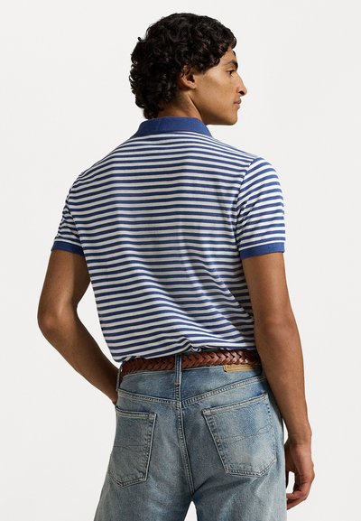 Pasiasta koszulka polo w niebiesko-białe paski, wykonana z bawełny, z jednolitym niebieskim kołnierzykiem. Noszona z jasnoniebieskimi jeansami i plecionym brązowym paskiem.