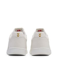 White leather sneakers featuring a smooth finish, gold accents, and a textured rubber sole; two chevron details on the heel.