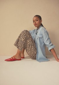 Chemise en denim bleu clair, pantalon beige avec motif léopard noir, et mules rouges à bout pointu. Textures lisses et contrastes de couleurs distincts.
