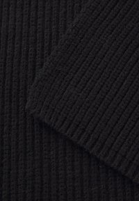 Sort tekstureret stof med lodret ribbning, der har bløde, fuzzy fibre. Stoffet er tykt og tæt, velegnet til varme beklædningsgenstande.