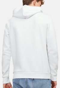 Hvid hættetrøje med en kængurulomme, ribbede manchetter og kant, samt en snor i hætten, parret med lyseblå denimjeans.