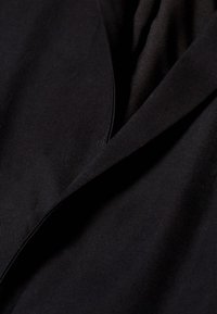 Svart tyg med en slät textur, med en vikt design och sned krage. Inga mönster eller hårdvara synliga.