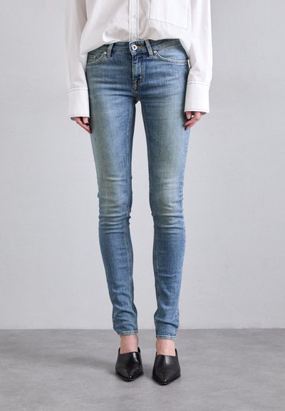 Tynne jeans i lyseblå denim med falmingdetaljer, parret med svarte spisse flate sko og en hvit oversized skjorte.