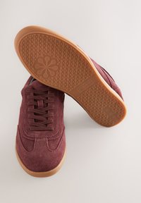 Zapatillas deportivas de ante burdeos oscuro con suela de goma texturizada, que cuentan con seis ojales, cordones planos y detalles de costuras en la parte superior.