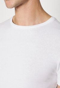 T-shirt bianco a maniche corte con collo rotondo, realizzato in tessuto di cotone morbido, con un design semplice e una leggera lucentezza.