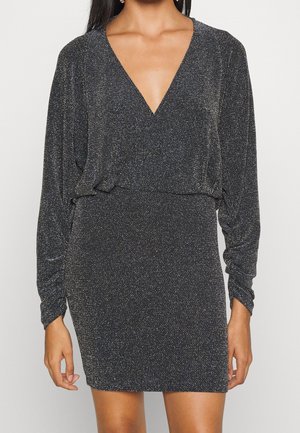 Schwarzes Kleid mit tiefem V-Ausschnitt, langen Ärmeln und taillierter Silhouette. Der Stoff hat eine strukturierte, glitzernde Oberfläche mit metallischen Akzenten.
