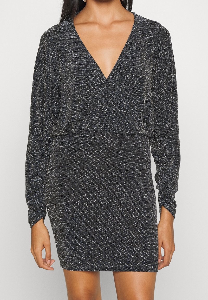 Svart klänning med djup V-ringning, långa ärmar och figursydd siluett. Tyget har en strukturerad glittrig finish med metalliska detaljer.