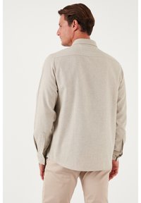 Maglietta a maniche lunghe color beige chiaro con una texture morbida, polsini con bottoni e colletto a punta. La vista posteriore mostra una vestibilità su misura e linee pulite.